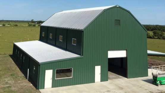 Big green gambrel metal barn with one fully enclosed leanto and one open leanto.